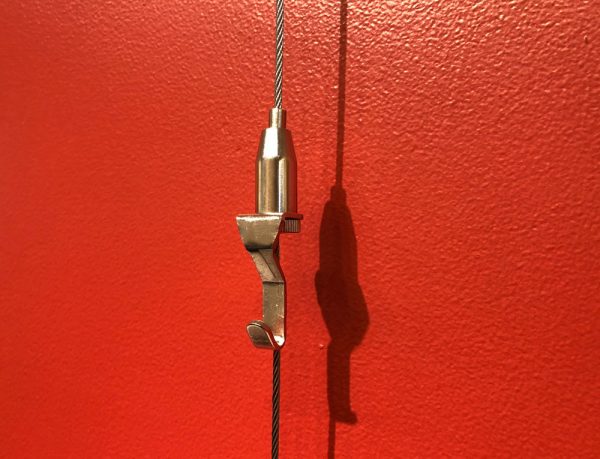 Self-gripping hook from MBS Standoffs for hanging artwork, can move up or down cable by pressing the button on top.